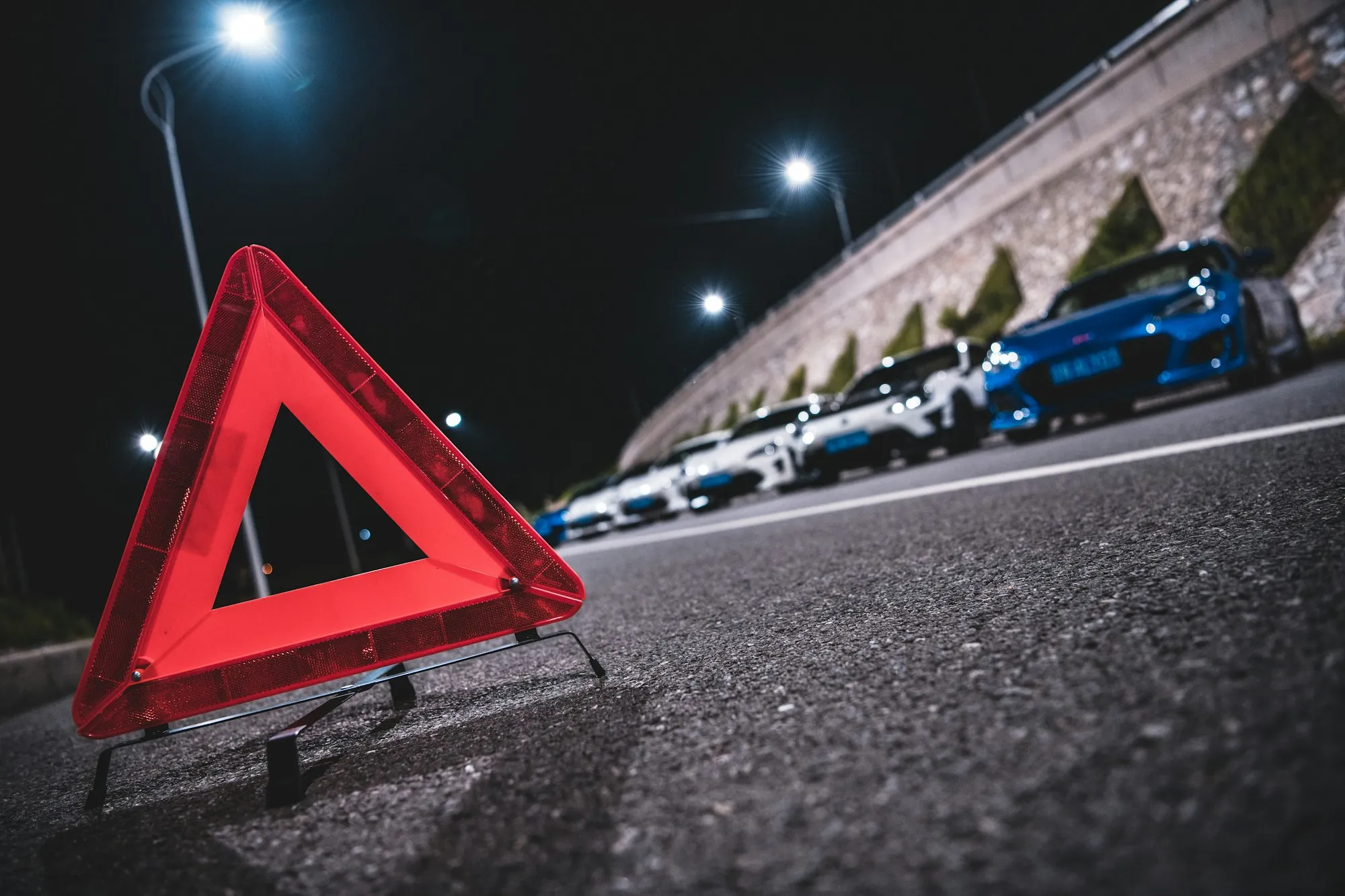 Red warning triangle placed on the pavement behind parked cars at night