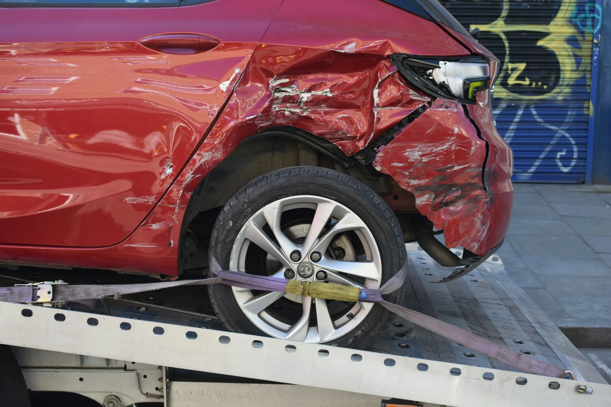 Damaged red car strapped by its wheels on the tilted deck of a flatbed tow truck