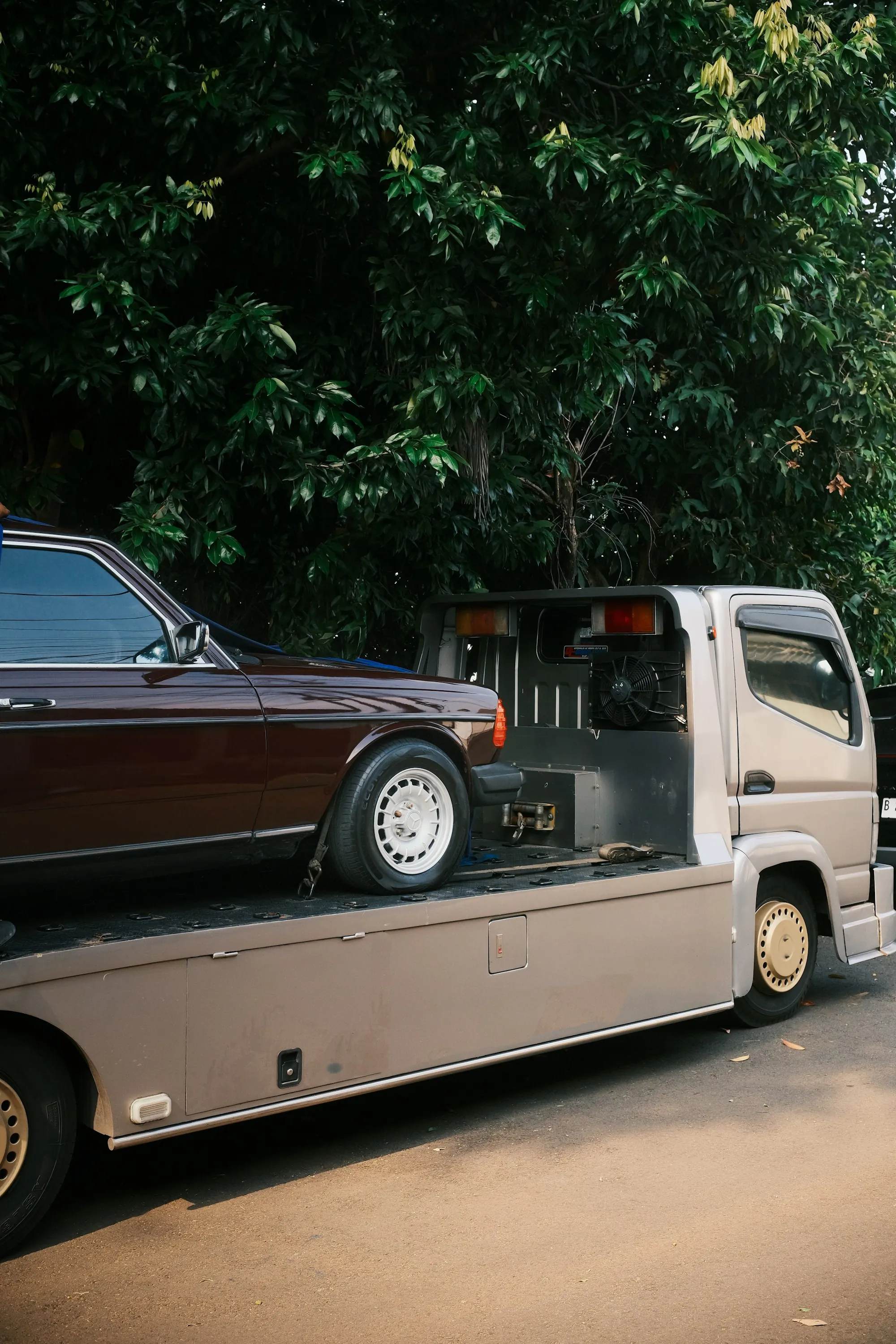 Sedan secured with straps on the bed of a flatbed tow truck