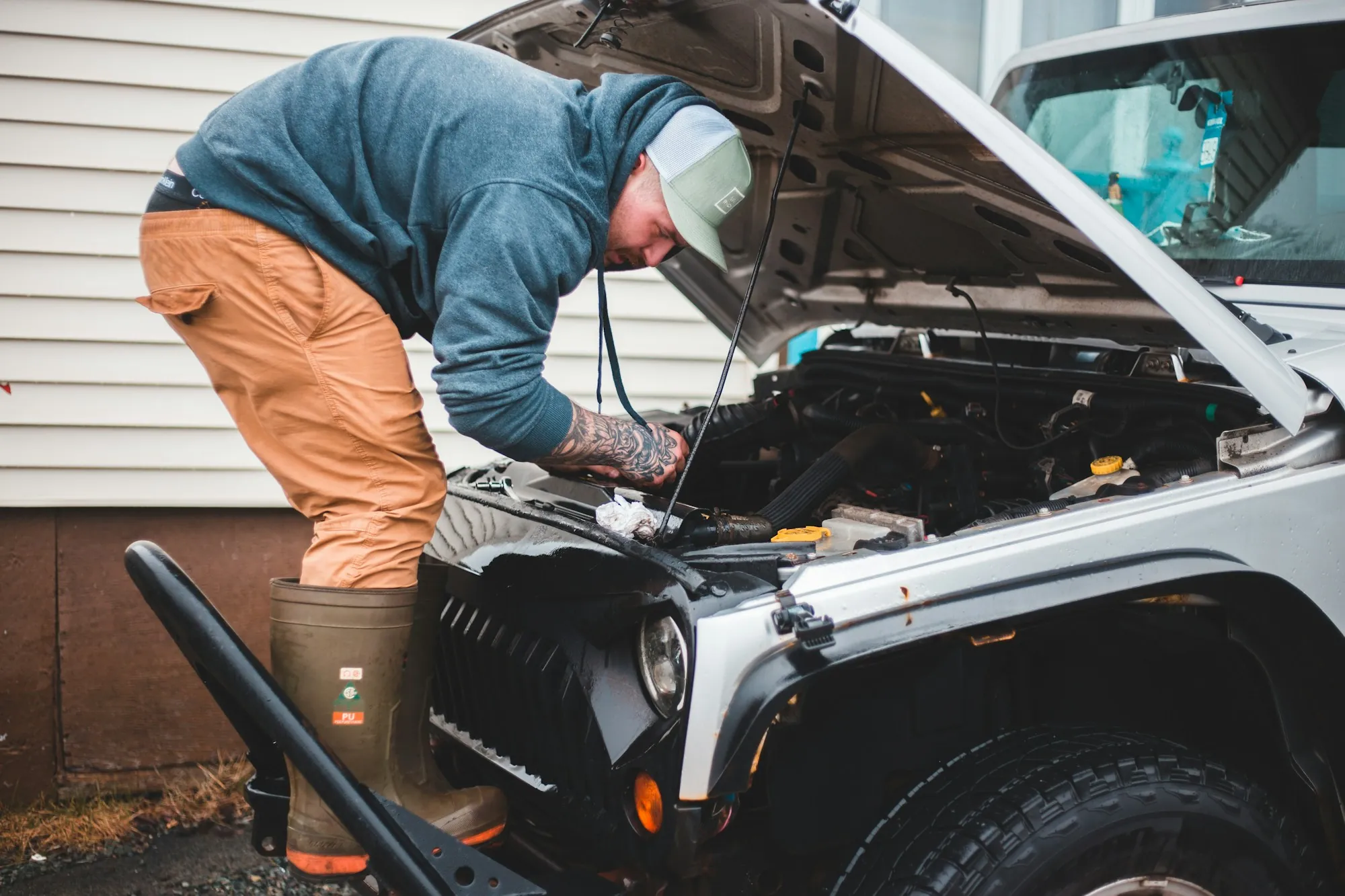 Roadside technician leaning under the open hood of a vehicle to diagnose a breakdown
