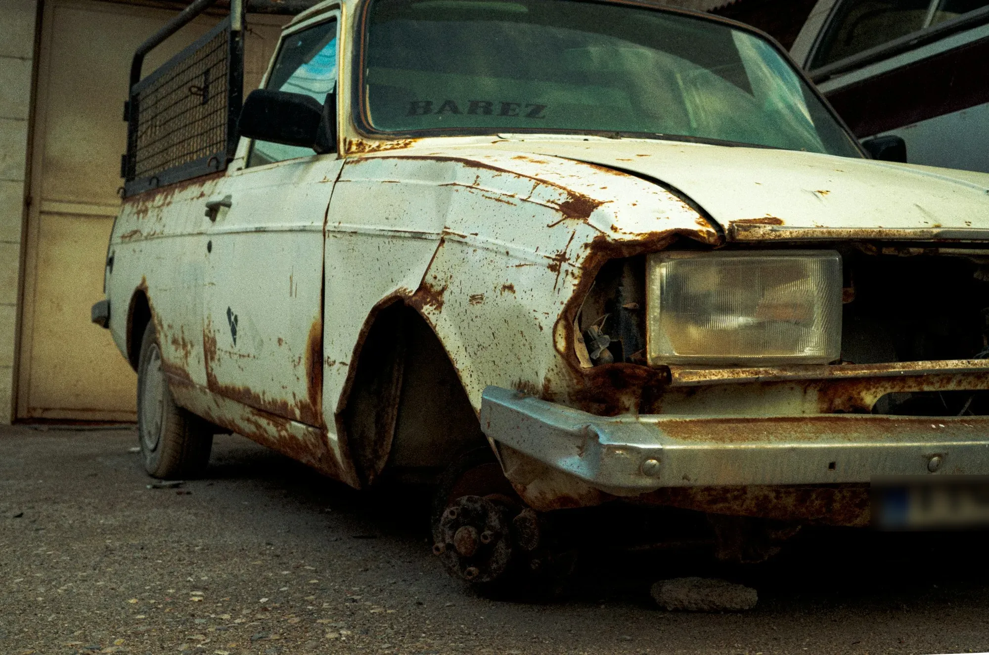 Rusted white car with a dented hood sitting under a carport