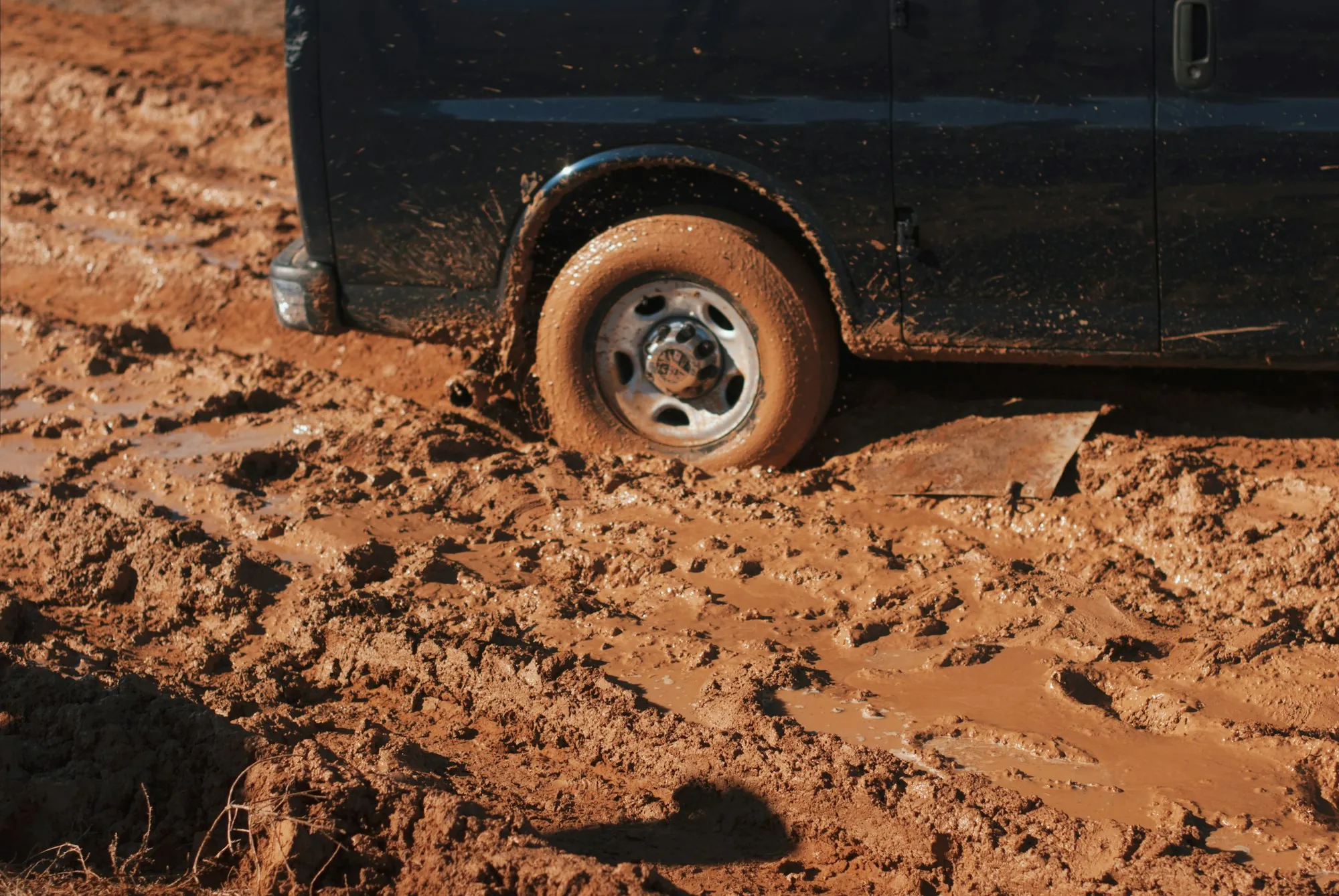 Van with its rear wheel sunk in thick red mud